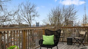 Um deck de madeira com uma cadeira preta e uma pequena mesa, com vista para o horizonte urbano.