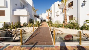A pathway leading through a white building complex with palm trees and a small water feature.