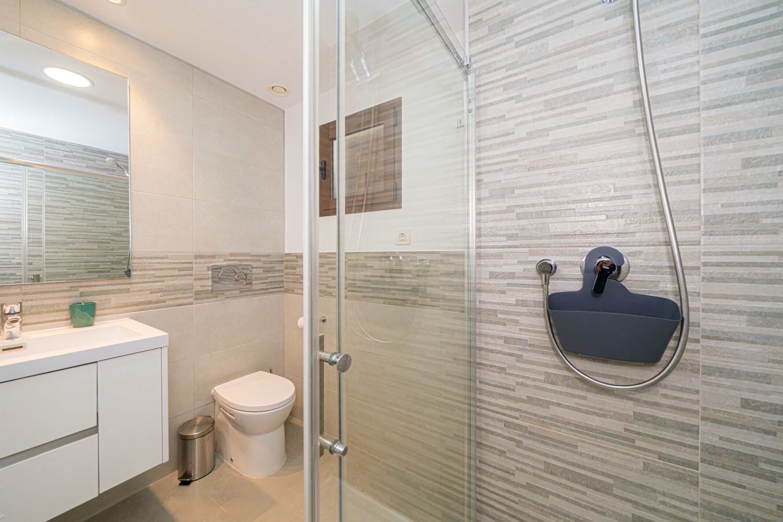 A modern bathroom with a glass shower enclosure, a white toilet, and a sink with a green soap dispenser.