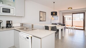 Een moderne keuken met een vaatwasser, magnetron en koffiezetapparaat. Er is een eethoek met een tafel en stoelen.