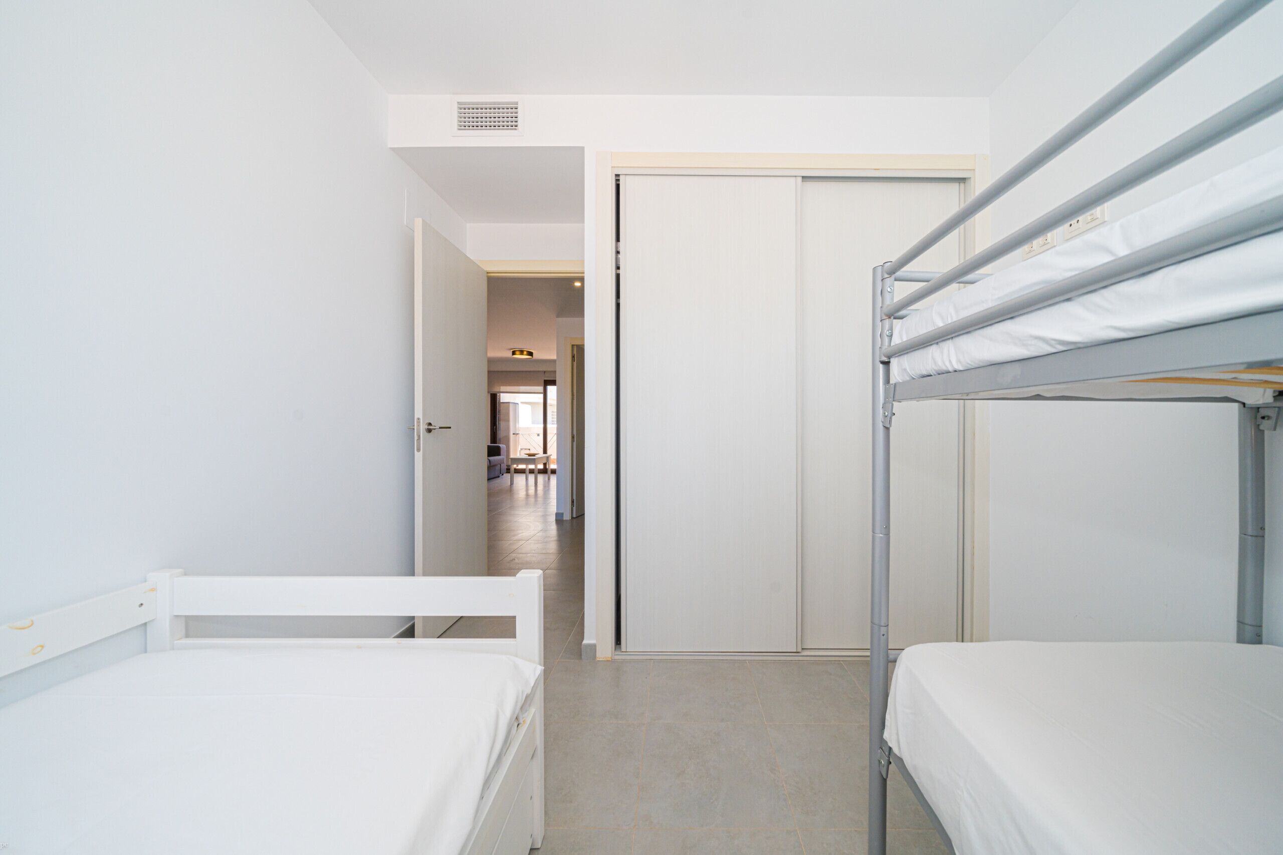 A room with bunk beds, a door, and a hallway leading to another room.