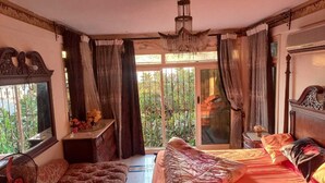 A bedroom with a large bed, a sofa, a small table, and a balcony with a view of greenery. - Villa Dr mohamed (Alexandria)