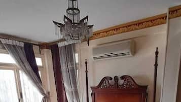 A bedroom with a large bed, a chandelier, curtains, and a tiled floor.