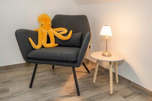 Un fauteuil gris avec un jouet en peluche représentant un poulpe jaune, une petite table ronde avec une lampe et un plancher en bois.