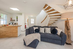 Un salon moderne avec un canapé gris, un escalier en bois et un coin cuisine.