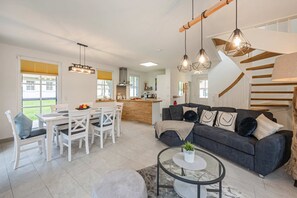 Un salon moderne avec un canapé gris, une table à manger blanche et une cuisine en arrière-plan.