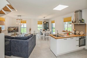 Une cuisine moderne avec un îlot central, un coin repas avec des chaises blanches et un canapé gris.