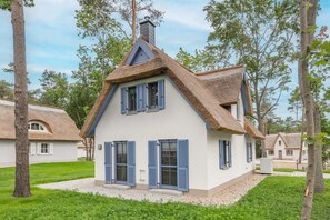 Une maison traditionnelle avec un toit de chaume très pentu, des murs blancs et des volets bleus.