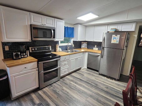 A modern kitchen with white cabinets, stainless steel appliances, a microwave, toaster, oven, and a refrigerator.. Coastal Cabin Retreat