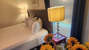 Ein ordentlich bezogenes Bett mit Kissen, einer Nachttischlampe und einer Vase mit Sonnenblumen.