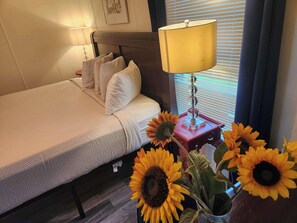 A neatly made bed with pillows, a bedside lamp, and a vase with sunflowers.