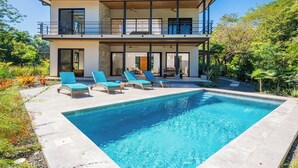 Una casa de dos pisos con piscina, mobiliario exterior y jardín.