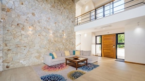 Un salón espacioso con una pared de piedra, un sofá de tonos claros, una mesa de centro de madera y una alfombra colorida.