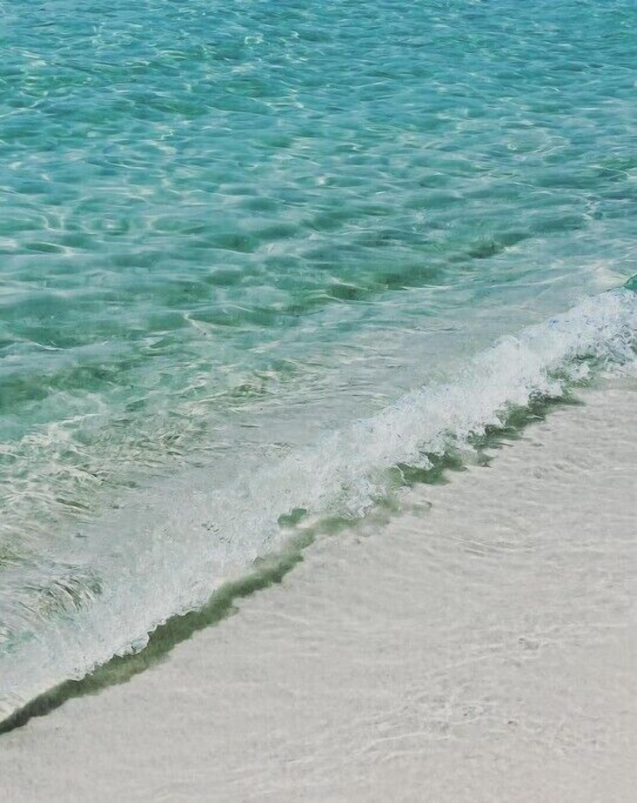 Clear turquoise water with gentle waves meeting a sandy beach.
