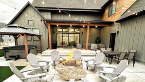 Een terras buiten met Adirondack stoelen rond een vuurkorf van steen, een overdekte zithoek en een barbecue.