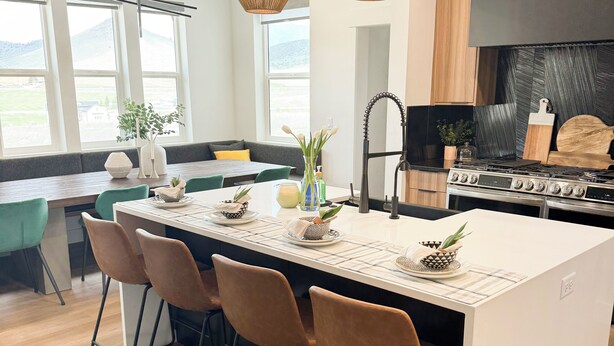 Een moderne keuken met een centraal eiland, barkrukken, hanglampen en uitzicht op het buiten.