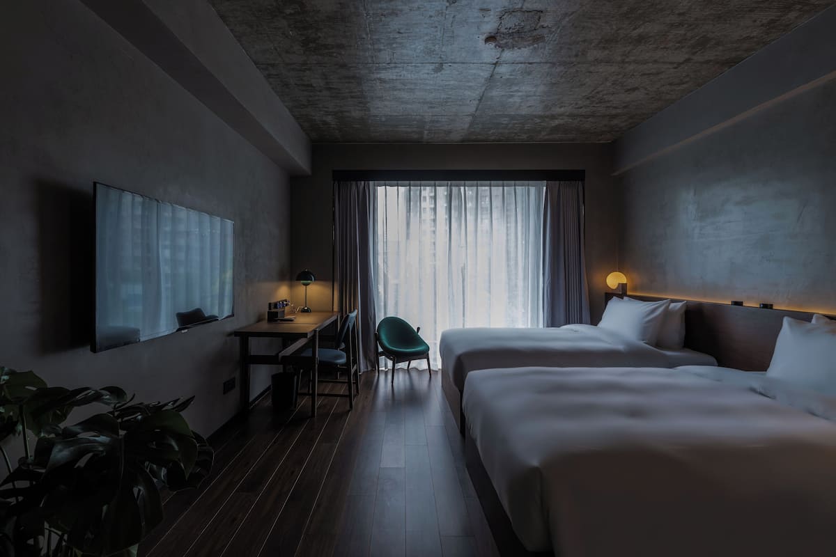 A hotel room with a bed, a desk, a chair, a TV, and a window with curtains.
