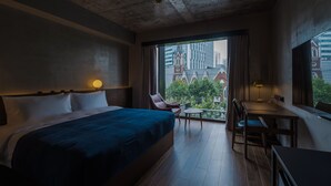 Habitación de hotel con una cama grande, un escritorio y una silla. Se ve un paisaje urbano a través de la ventana.