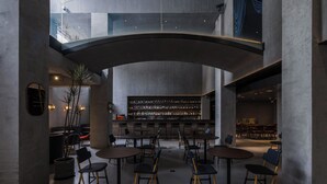Un interior espacioso con una zona de bar central, varios arreglos de asientos y un techo alto con estructura de vidrio.