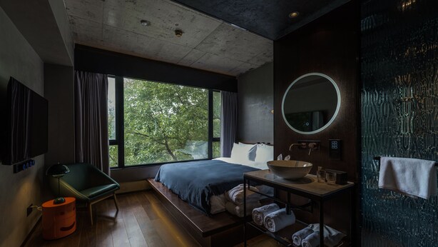 Un dormitorio moderno con un ventanal grande, una cama, una mesita de noche con lavabo y un espejo.