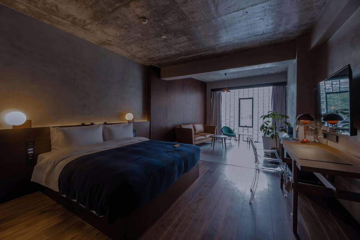 A modern hotel room with a large bed, a desk, a chair, and a view of the outdoors.