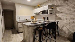 Cocina moderna con pared de ladrillo, armarios blancos y una barra con taburetes.