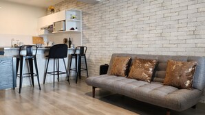 Un espacio de estar moderno con un sofá gris, sillas negras y una cocina al fondo.