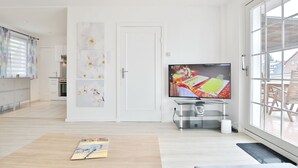Ein modernes Wohnzimmer mit einem großen Flachbildfernseher, einem Holztisch und Blick ins Freie durch ein großes Fenster.