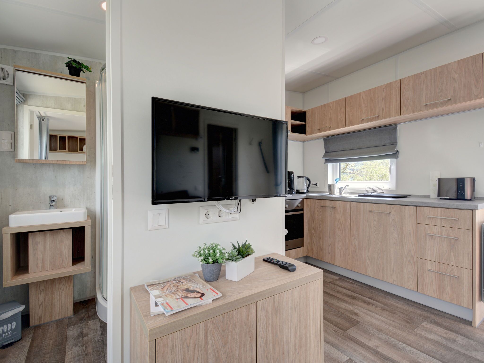 A modern kitchen with wooden cabinets, a built-in TV, and a countertop with a remote control.