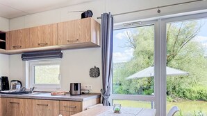 Une cuisine moderne avec des meubles en bois, une table à manger avec une chaise, une machine à café et une bouilloire.
