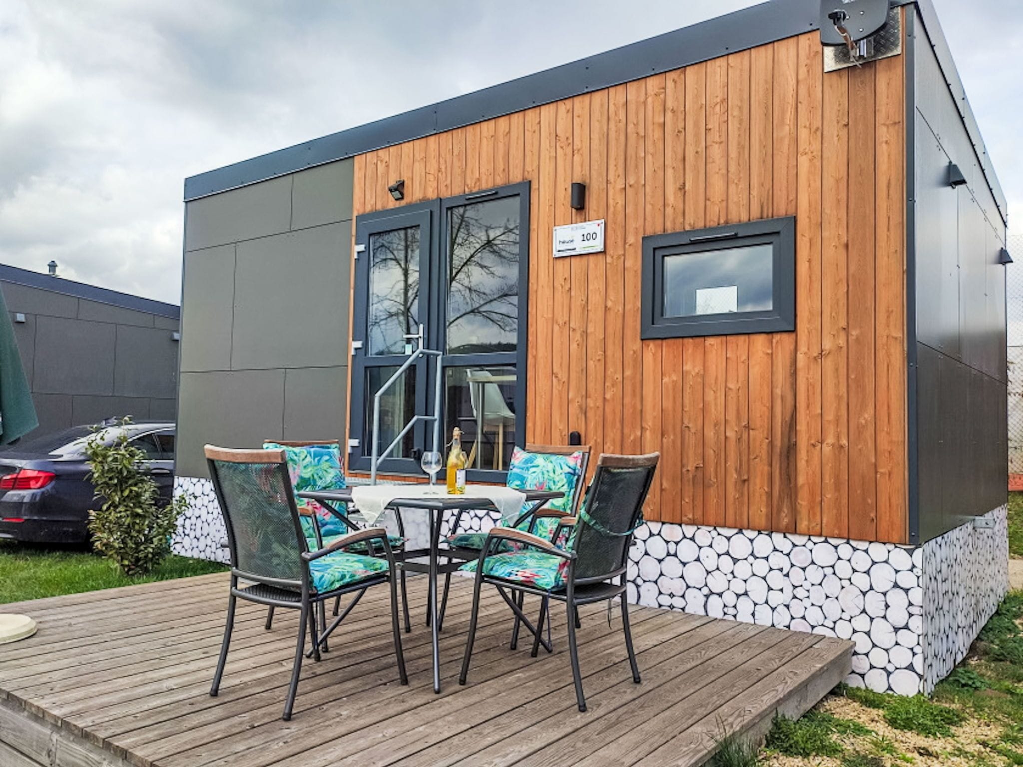 Un bâtiment moderne doté d’une façade en bois et d’une base en pierre. On y trouve une terrasse avec des sièges d’extérieur et une bouteille de champagne.