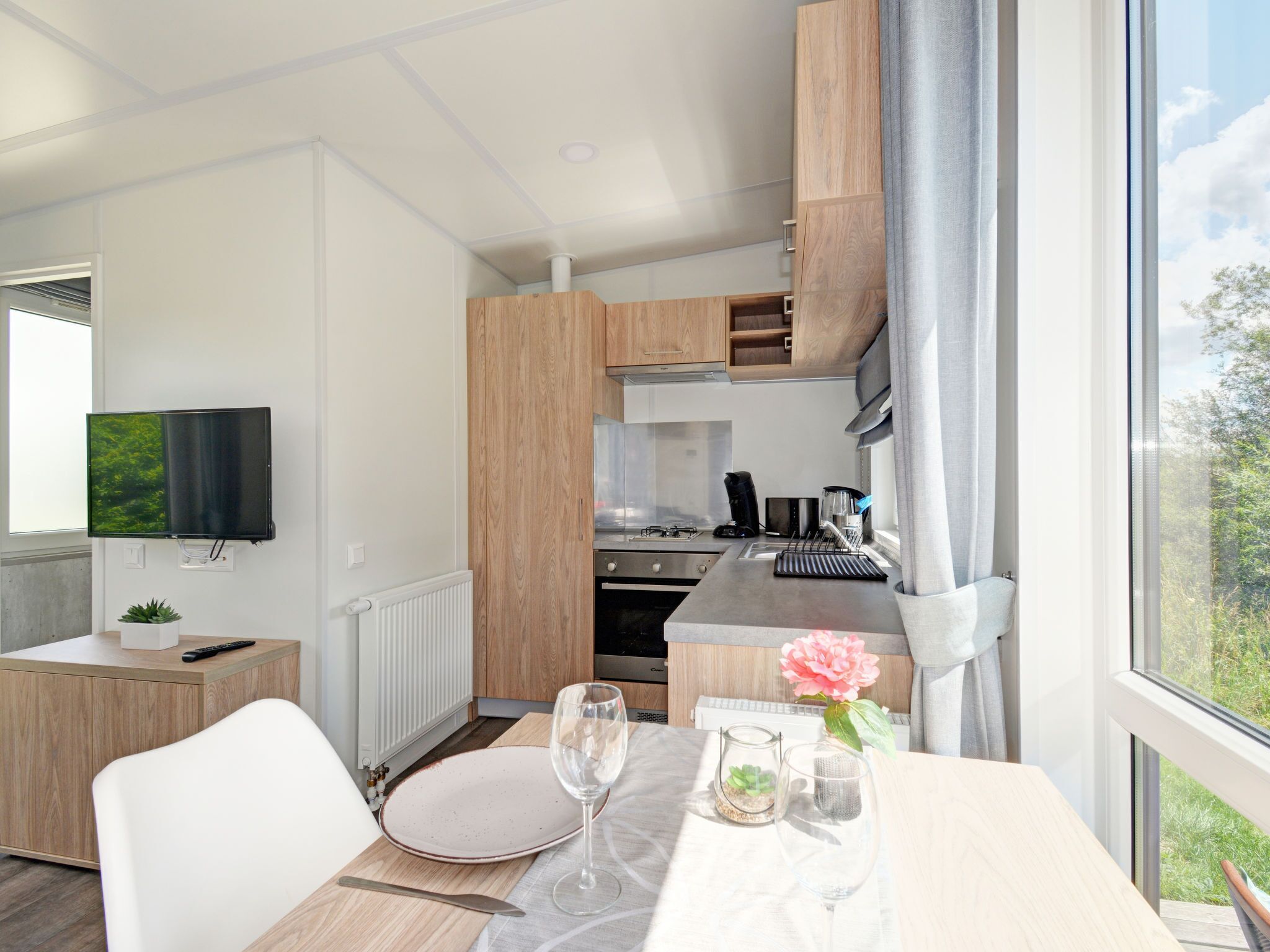 A modern kitchen with wooden cabinets, a built-in oven, and a window with a view of greenery.