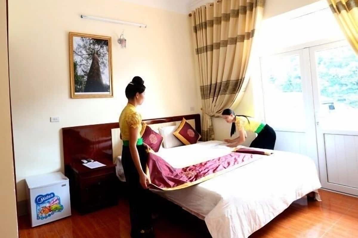 A hotel room with a bed, a nightstand, a bedside table, a picture on the wall, and a window with curtains.