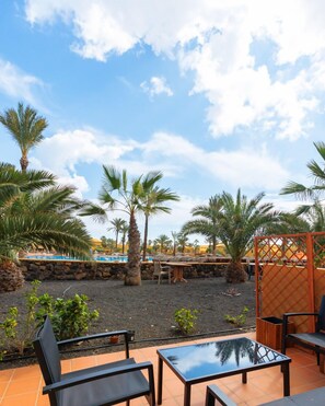 Eine Terrasse im Freien mit einem Glastisch und Stühlen, umgeben von Palmen und einem Pool im Hintergrund.