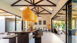 A spacious dining area with a long wooden table, benches, and hanging wicker lamps. - Ibumah Villa Bingin (Pecatu)