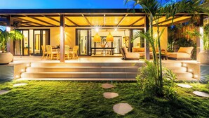 A modern outdoor patio with a dining area, steps leading to a covered seating area, and tropical plants. - Ibumah Villa Bingin (Pecatu)
