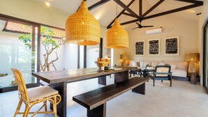 A modern living room with a wooden dining table, wicker chairs, a bench, and a ceiling fan. - Ibumah Villa Bingin (Pecatu)