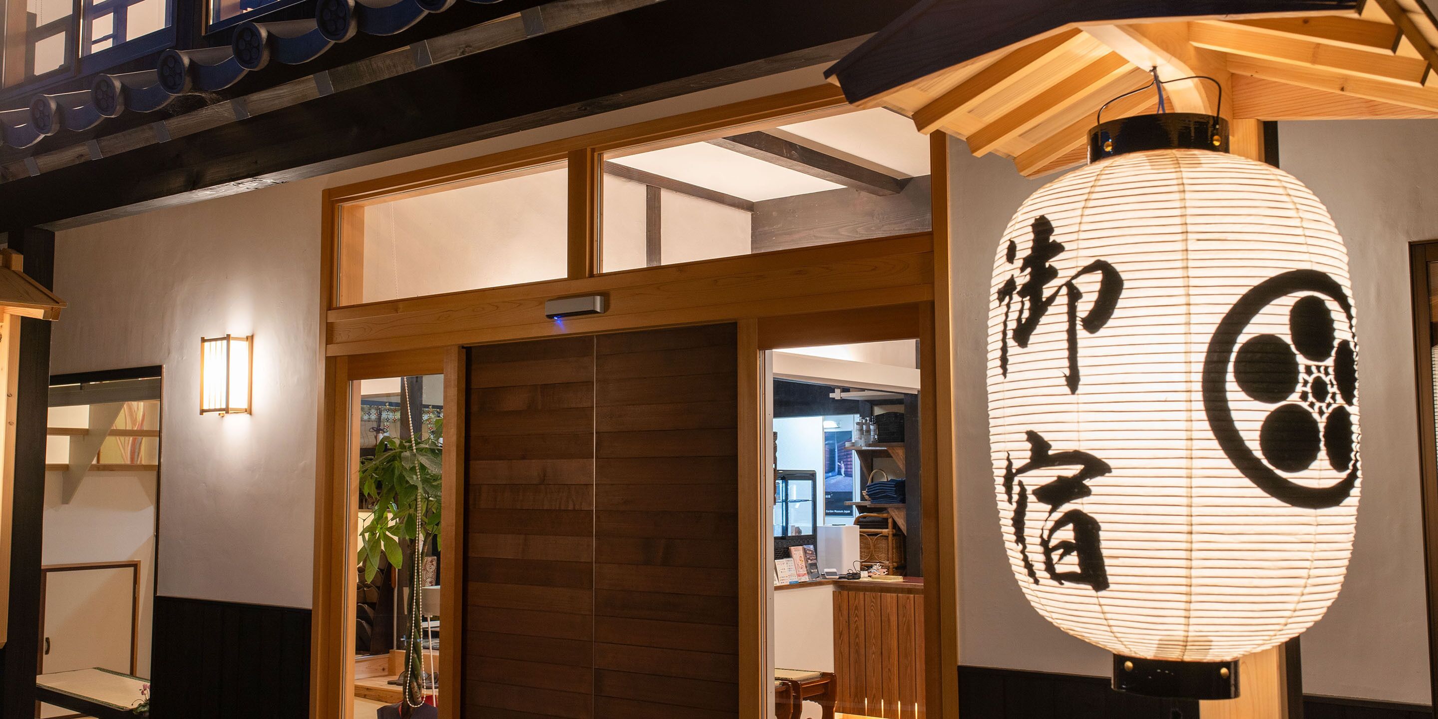 Un edificio japonés tradicional con fachada de madera, una puerta corredera y un farol de papel colgante con caracteres japoneses.