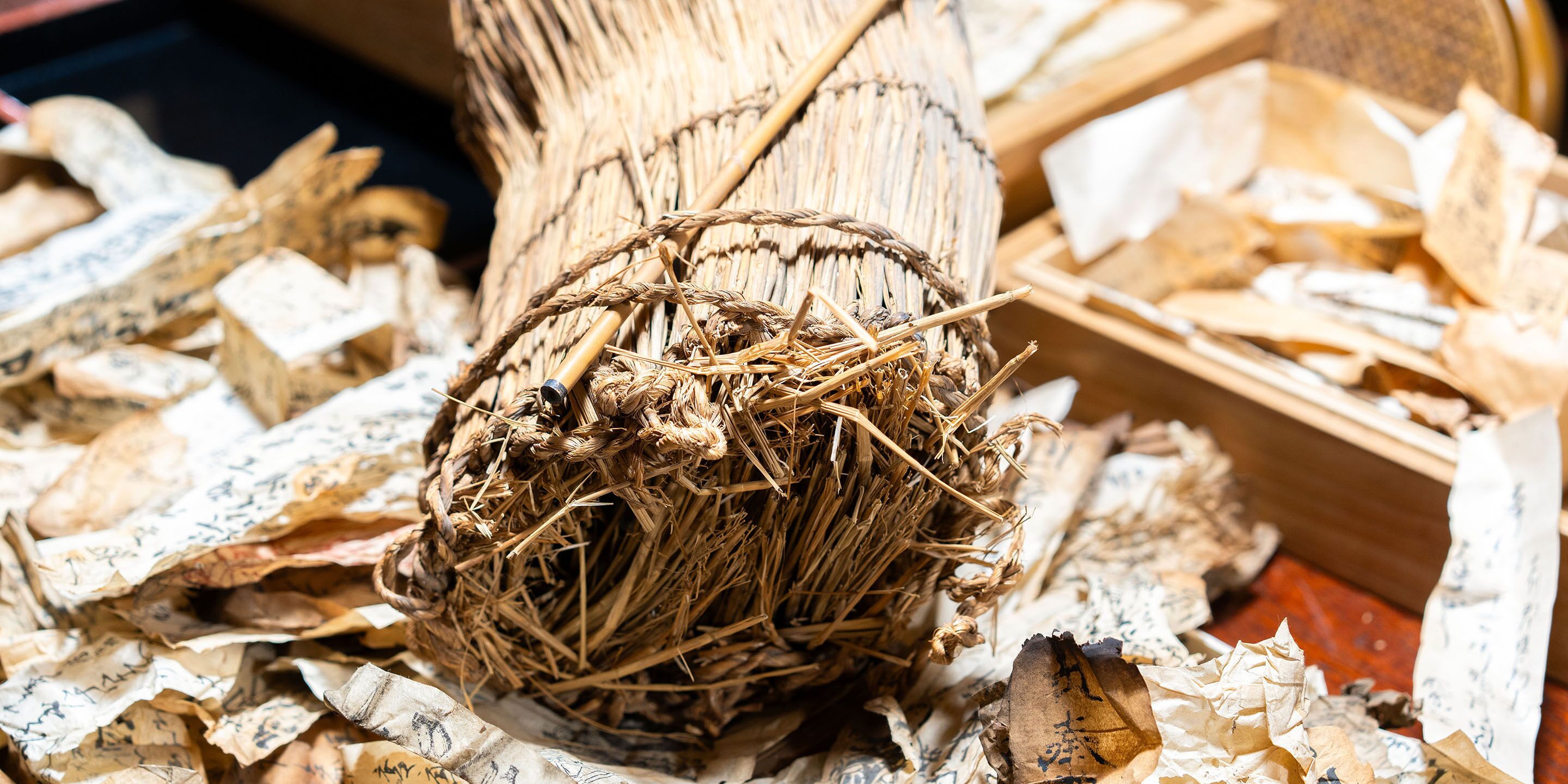 A close-up of a bundle of dried straw or hay tied with a rope, surrounded by scattered wood shavings.