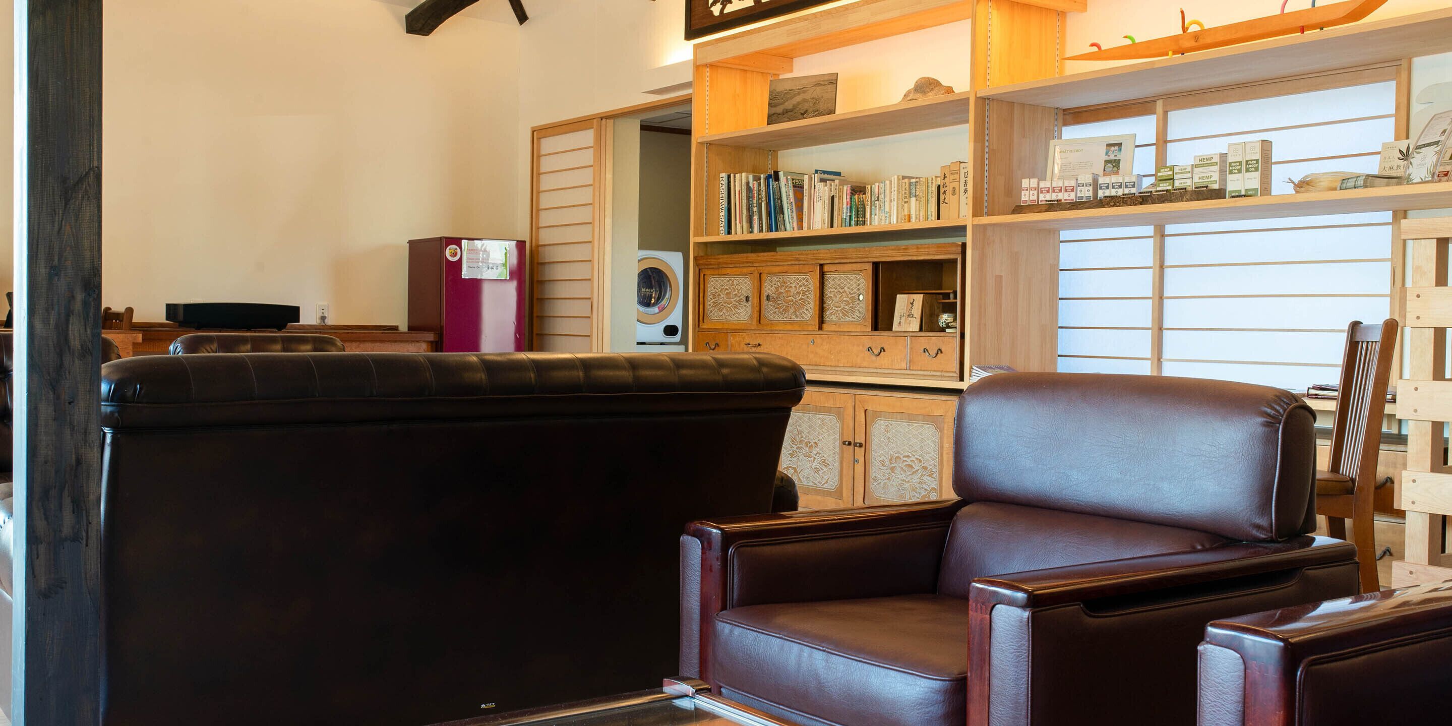 A living room with a dark brown leather sofa, a wooden cabinet with books and decorative items, and a washing machine.