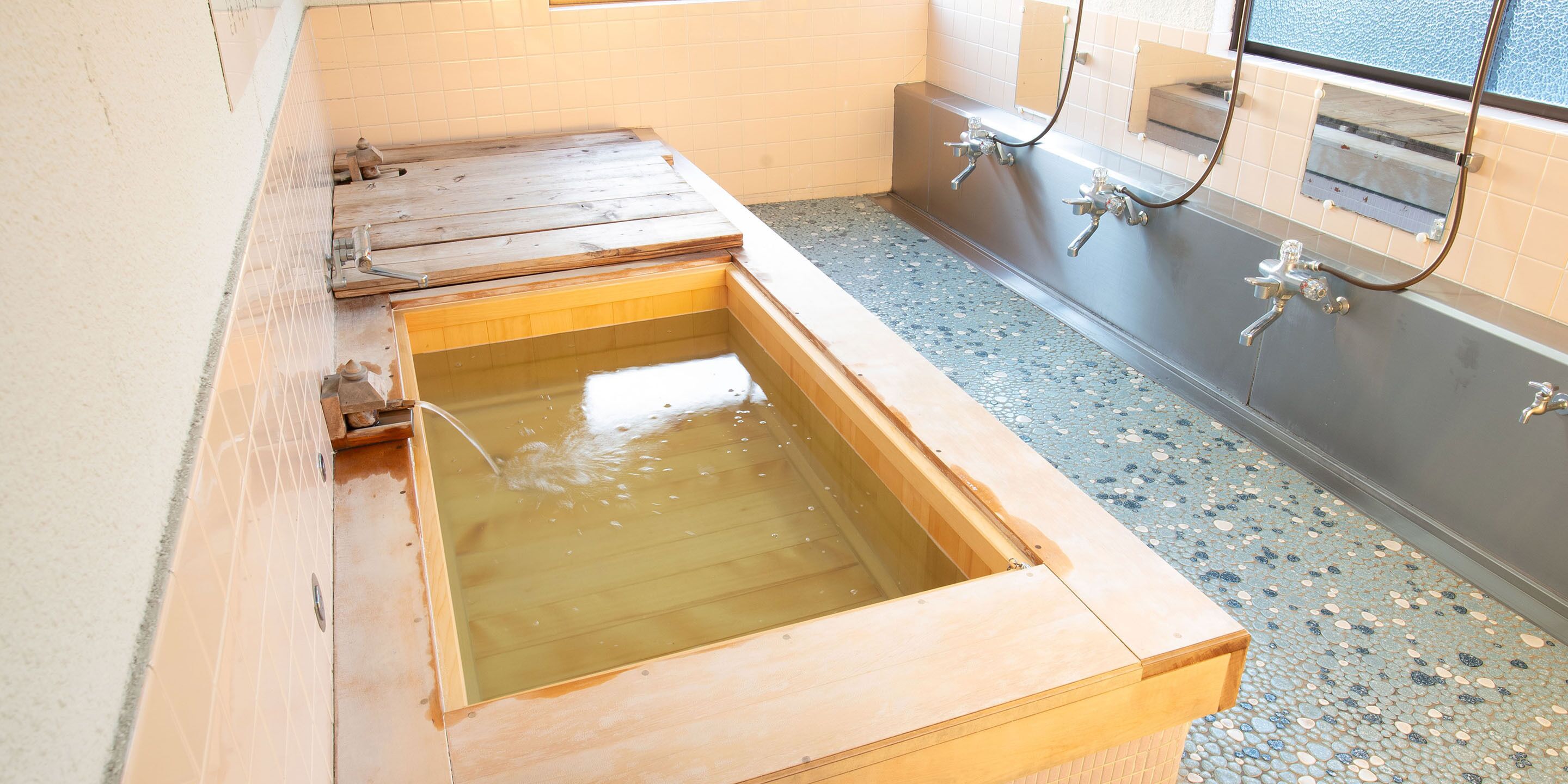 A wooden bathtub with a tiled floor and a window above it.