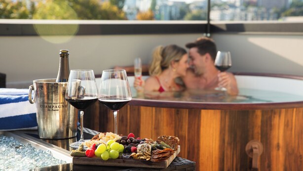 A hot tub with a city view, a bottle of champagne, two wine glasses, and a charcuterie board with fruits and cheeses. - The Emerald Den (Seattle)