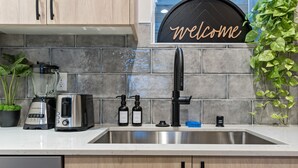 A kitchen with a stainless steel sink, wooden cabinets, a toaster, a blender, and a 'Welcome' sign. - The Emerald Den (Seattle)