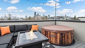 A rooftop terrace with a black sofa, a table with a fire feature, and a wooden hot tub. - The Emerald Den (Seattle)