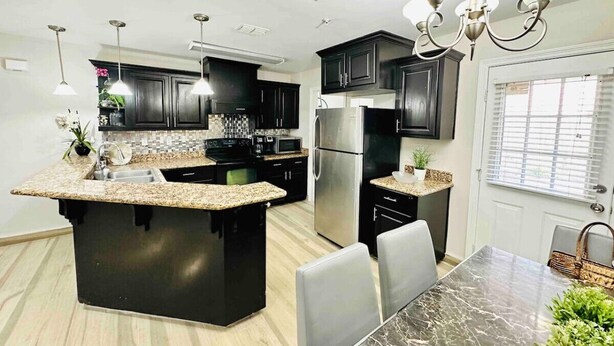 A modern kitchen with granite countertops, dark cabinetry, stainless steel appliances, and a dining area with a marble table. - Sharyland Townhome - 2/2.5 bedrooms with patio in McAllen (McAllen)