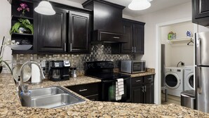 A kitchen with dark cabinets, a granite countertop, a coffee maker, a microwave, and a built-in washer and dryer. - Sharyland Townhome - 2/2.5 bedrooms with patio in McAllen (McAllen)