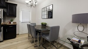 A modern kitchen with dark cabinets, a granite countertop, a dining table with four chairs, a chandelier, a mirror, and a glass table with a magazine. - Sharyland Townhome - 2/2.5 bedrooms with patio in McAllen (McAllen)