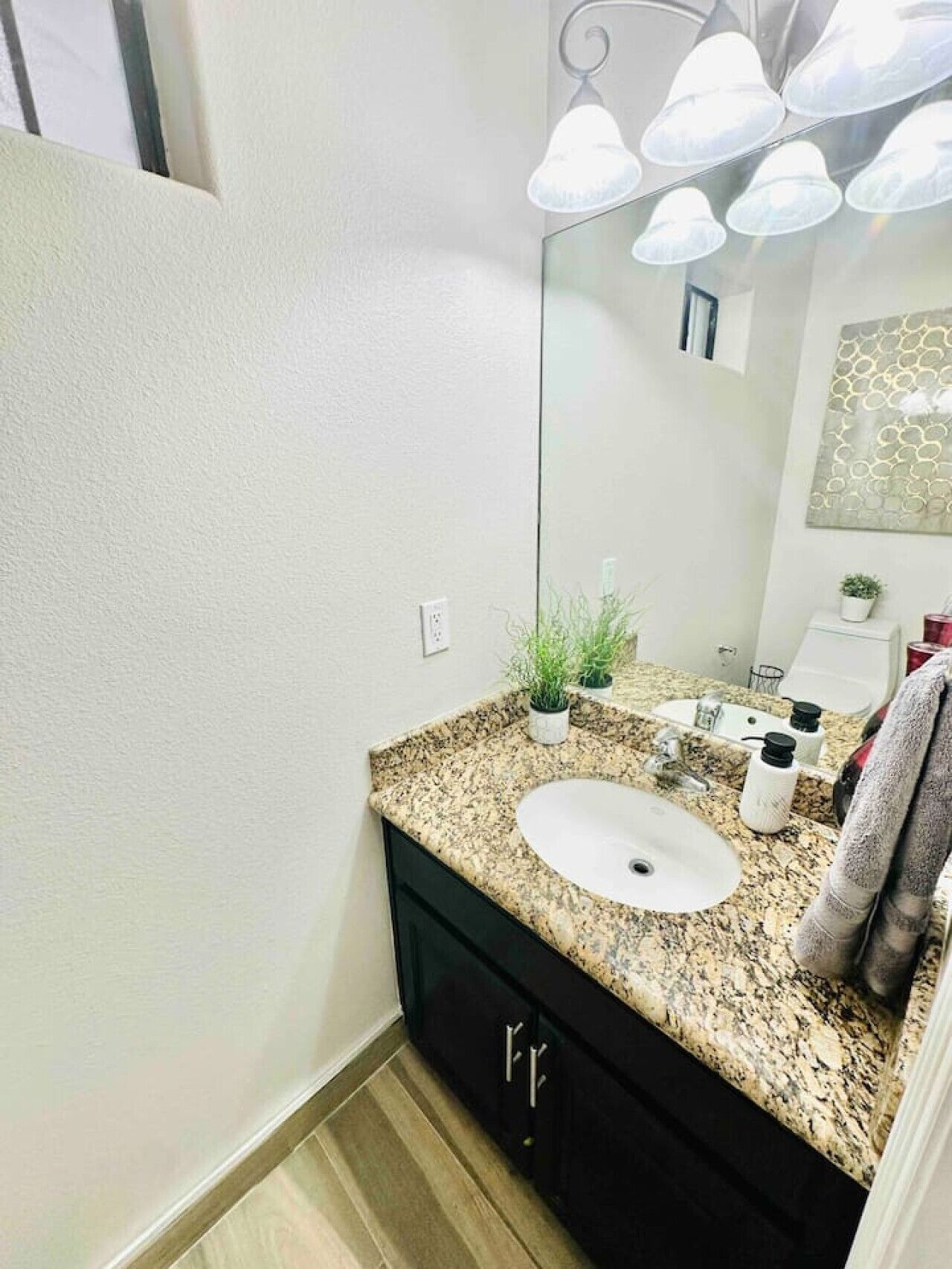 A modern bathroom with a granite countertop, a white sink, a black cabinet, a mirror, and a ceiling light fixture.