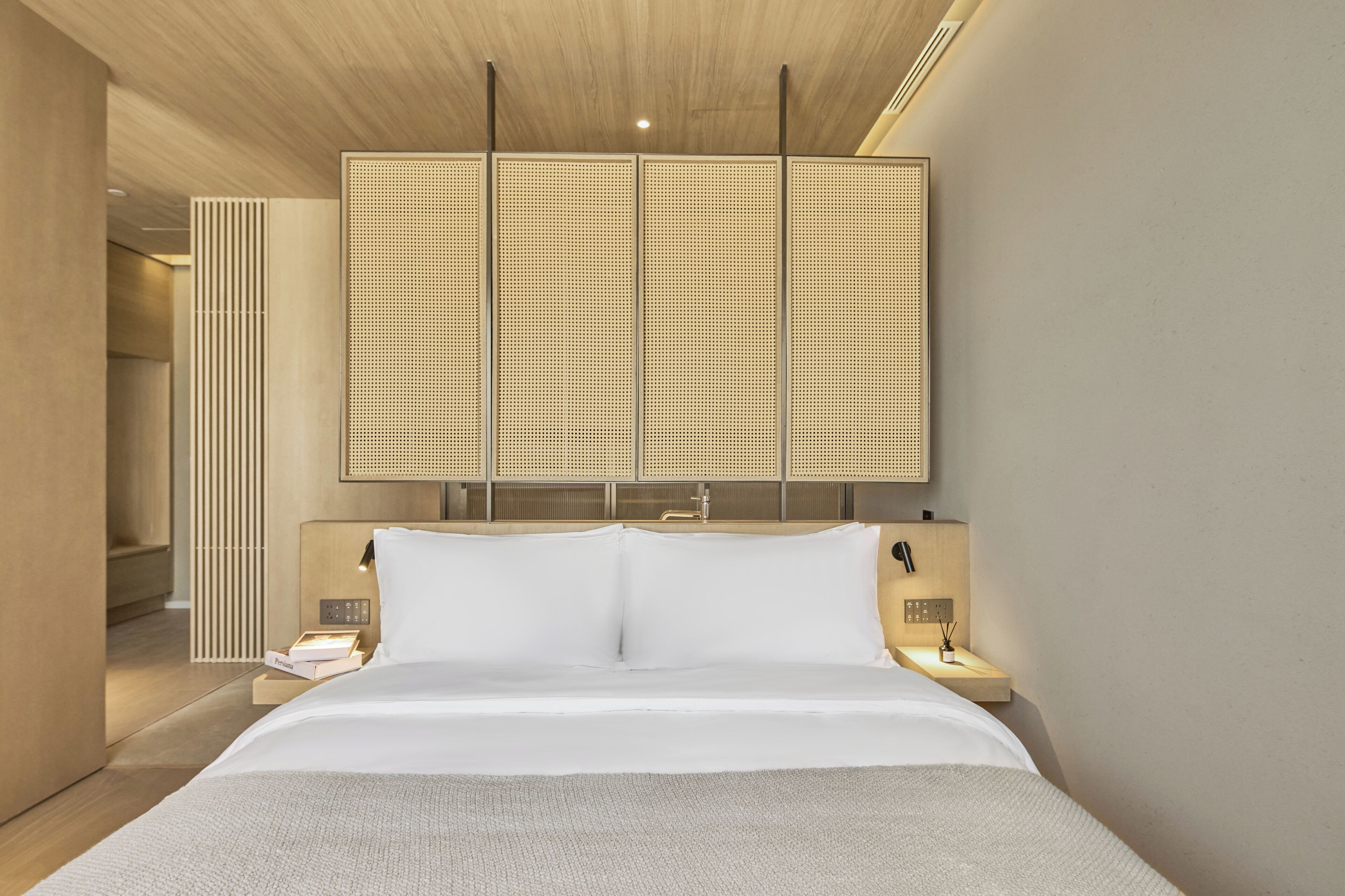 Een moderne hotelkamer met een groot bed, een houten hoofdeinde en een wandpaneel.
