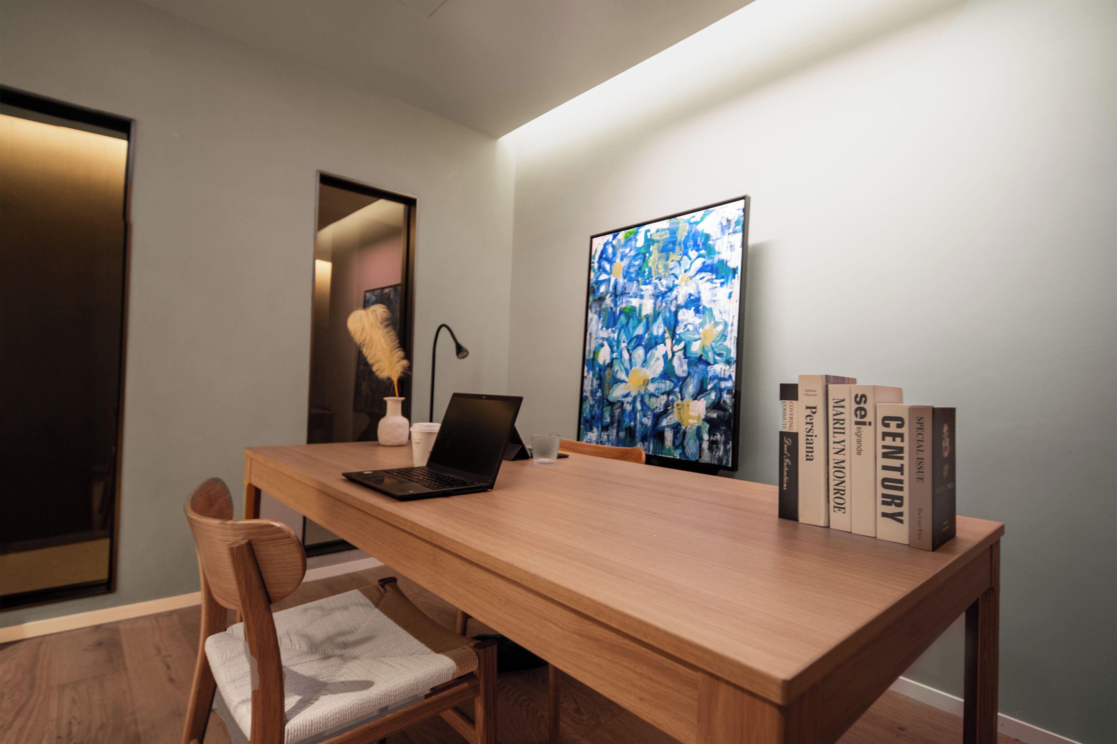 A modern room with a wooden desk, a laptop, a vase, and a bookshelf with books.
